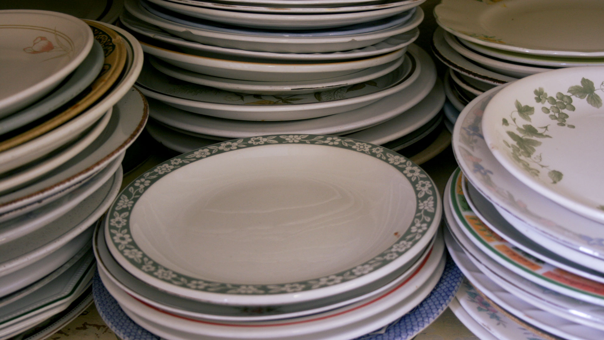 A stack of stacked plates with various designs including floral patterns, geometric patterns, and solid colors.
