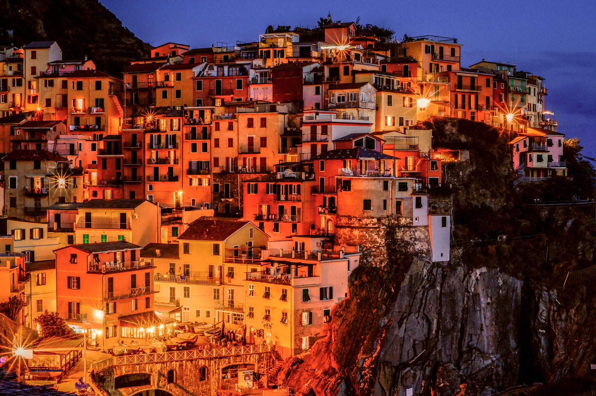 A hillside town built on terraced slopes is illuminated by warm-toned lights at night.